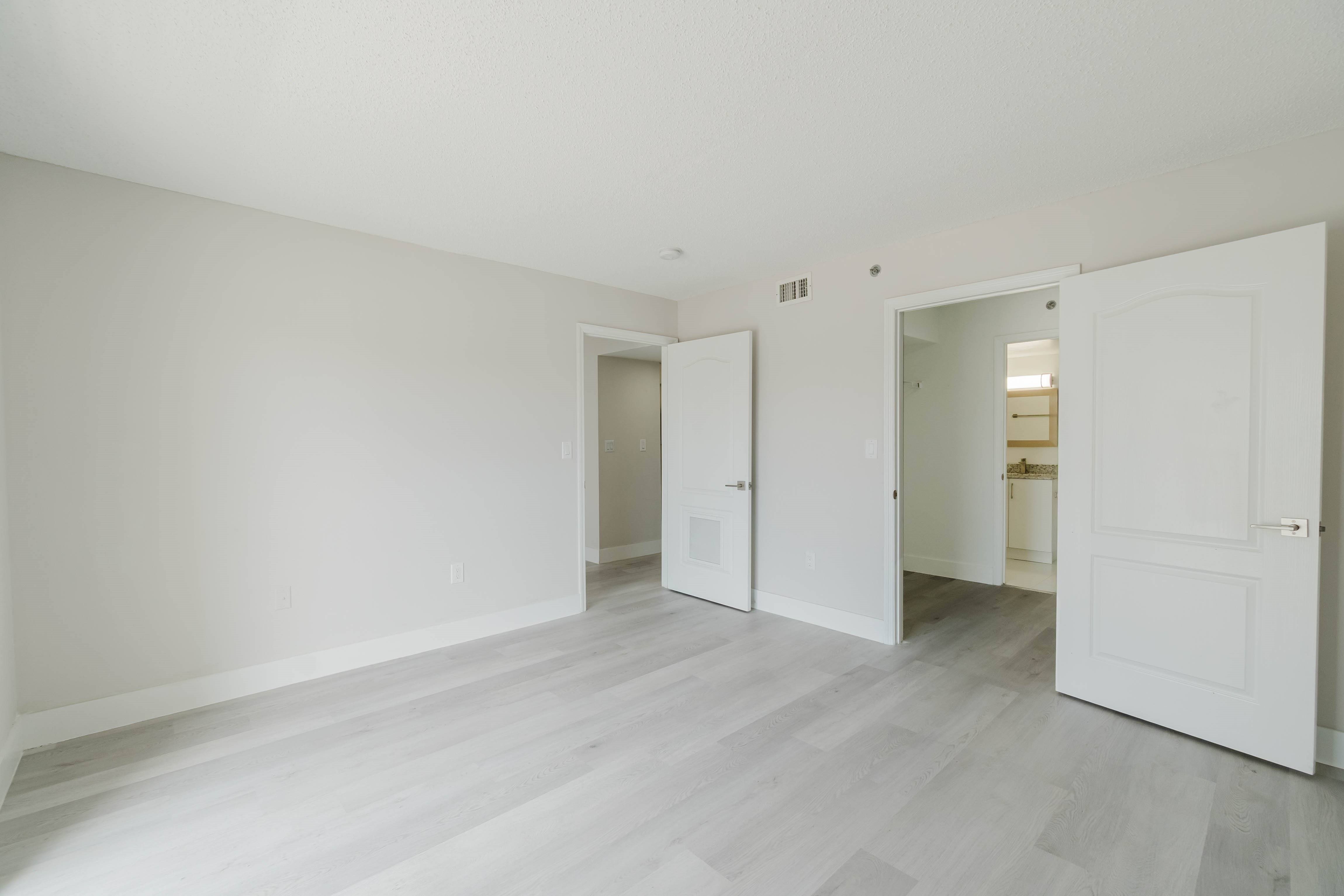A room with white walls and a grey floor with two white doors.